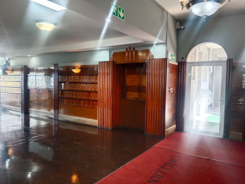 A well-maintained apartment building entrance lobby featuring classic wooden wall paneling, integrated mailboxes, and a glass-paneled main door with polished parquet flooring.