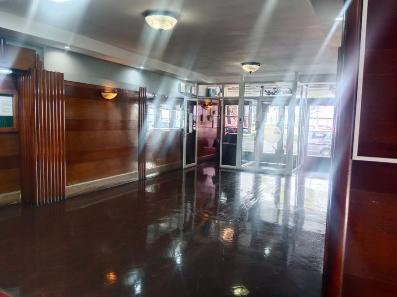 Spacious apartment building entrance lobby featuring polished flooring and classic wood wall paneling with glass entry doors.