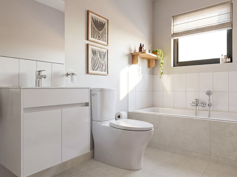 Modern bathroom featuring a clean white vanity, integrated basin, toilet, and a tiled bathtub with shower mixer, finished with neutral wall and floor tiles.