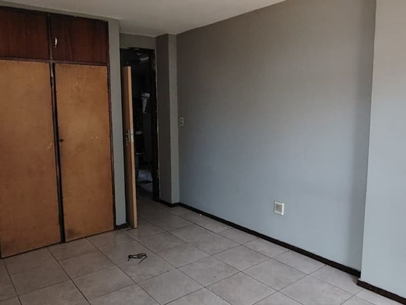 An empty bedroom featuring tiled flooring and dated built-in wooden cupboards, offering a blank canvas for renovation or restyling.