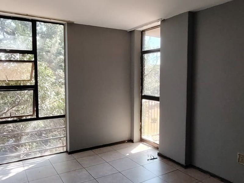 An empty bedroom featuring tiled flooring and large windows that provide ample natural light and views of the surrounding greenery.