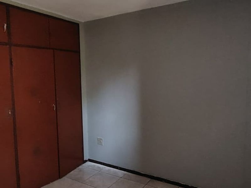 An empty bedroom featuring tiled flooring and built-in wooden cupboards, offering a blank canvas for potential interior updates.