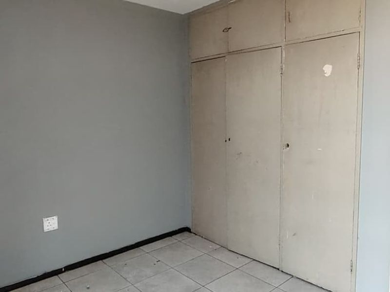 An empty bedroom featuring tiled flooring and built-in cupboards, requiring cosmetic updates to the walls and cabinetry to improve its overall appeal.