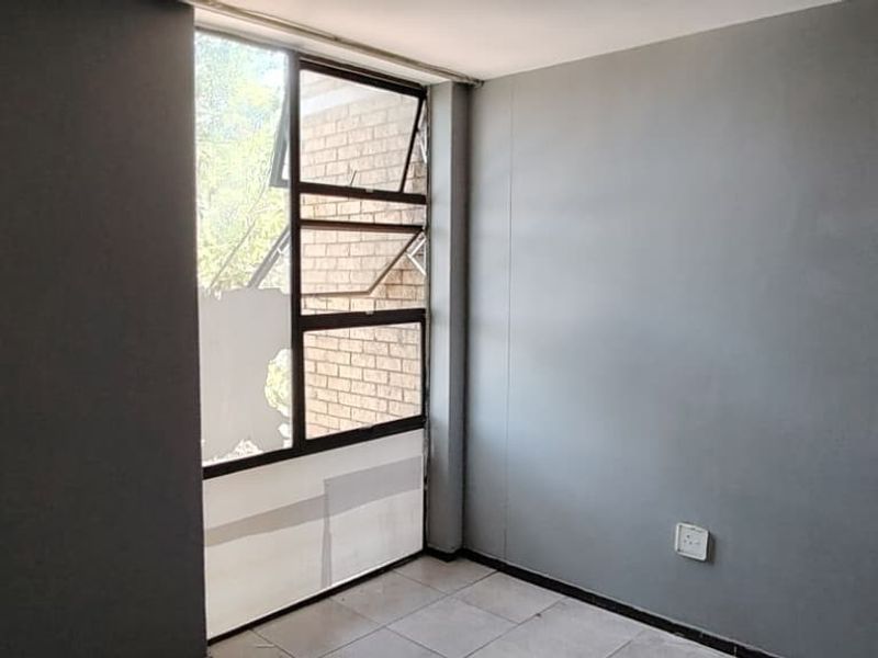 An empty bedroom featuring grey painted walls, tiled flooring, and a large window with visible damage to the glass and film.
