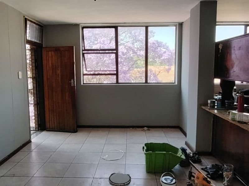 An open-plan living and kitchen area featuring tiled flooring, large windows, and a built-in kitchen counter, offering a blank canvas for renovation.