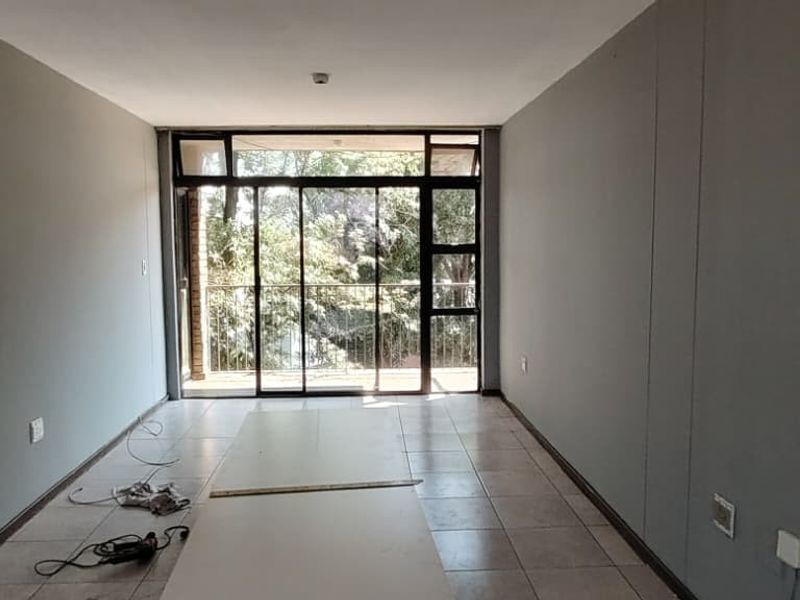 An empty, neutrally painted living area featuring tiled flooring and large sliding glass doors that provide access to an outdoor balcony.