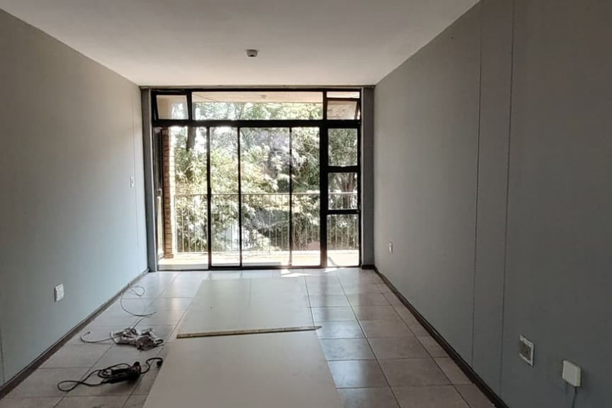 An empty, neutrally painted living area featuring tiled flooring and large sliding glass doors that provide access to an outdoor balcony.