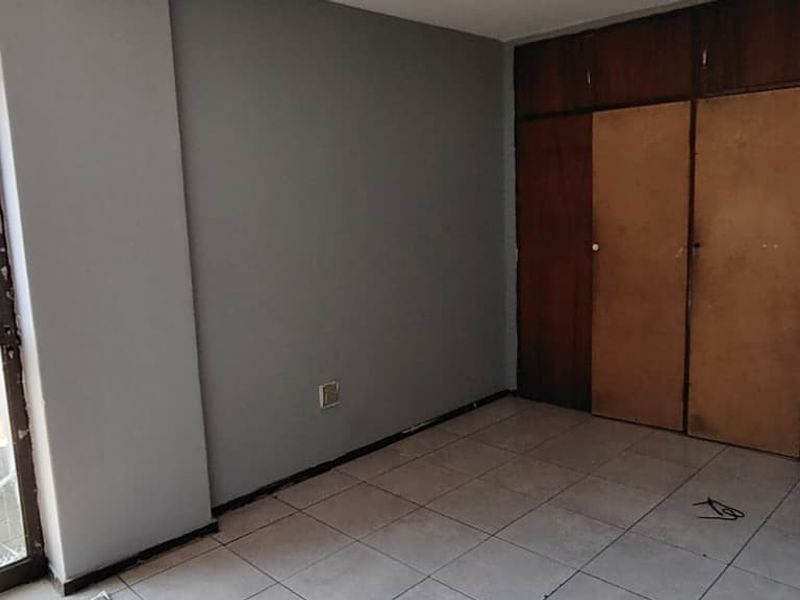 An empty bedroom featuring tiled flooring, built-in wooden cupboards, and a sliding glass door leading to an outdoor area.