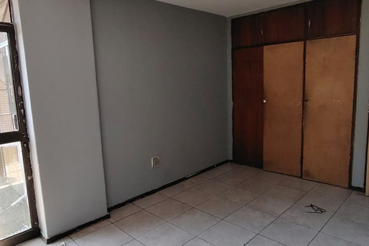 An empty bedroom featuring tiled flooring, built-in wooden cupboards, and a sliding glass door leading to an outdoor area.