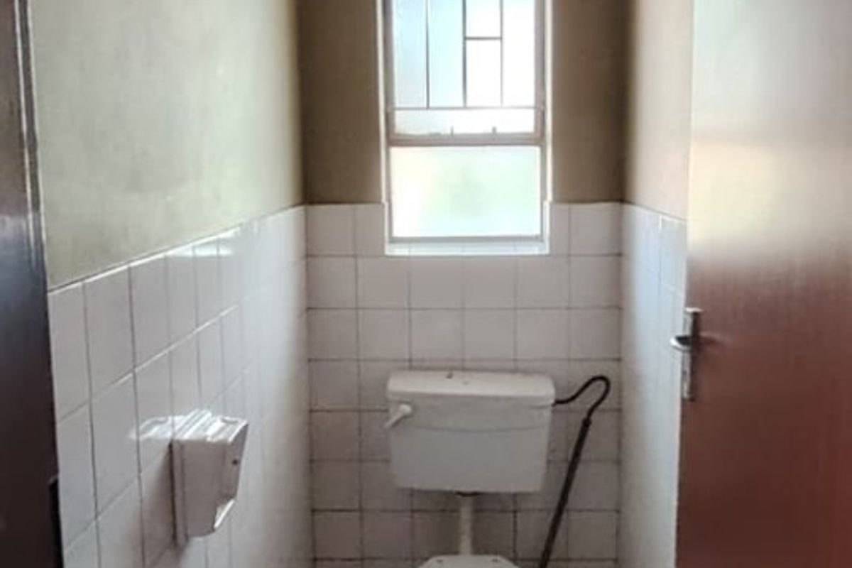 A compact, functional bathroom featuring a standard toilet, tiled walls, and tiled flooring, requiring cosmetic updates to improve its overall condition.