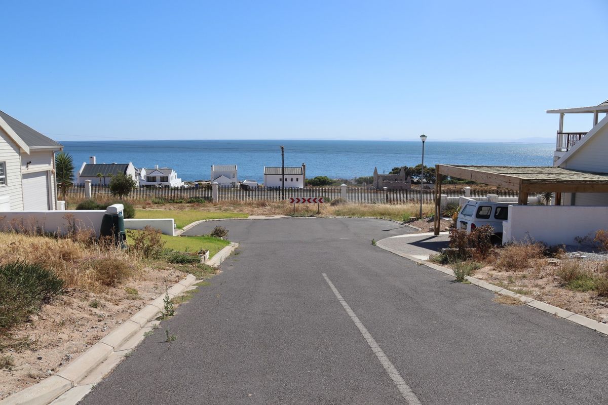 A street-level view of a residential access road leading towards a coastal area with ocean views and surrounding residential properties.