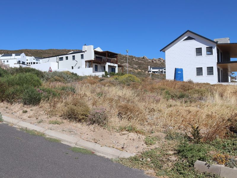 A view of a vacant residential plot from the street, featuring natural vegetation and surrounding residential properties.