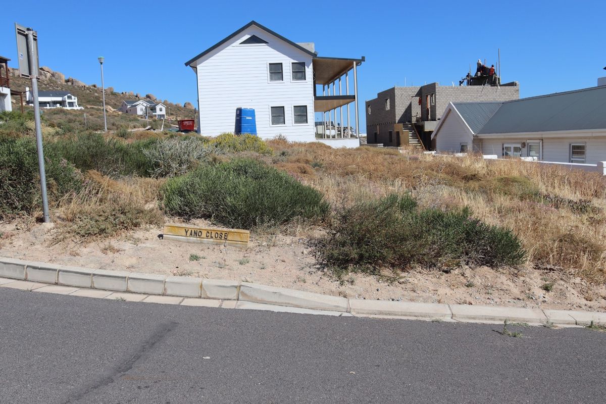 Street view of a vacant residential plot featuring natural coastal vegetation, concrete kerbing, and adjacent residential development.