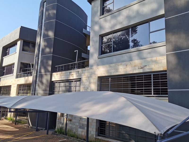 Modern multi-story office building exterior featuring stone cladding, glass block accents, and integrated shade sail parking structures.