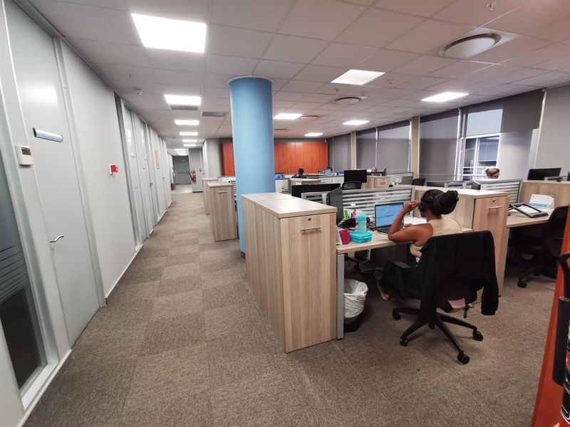 A professional open-plan office space featuring carpeted flooring, suspended ceilings with recessed lighting, and integrated workstation cabinetry.