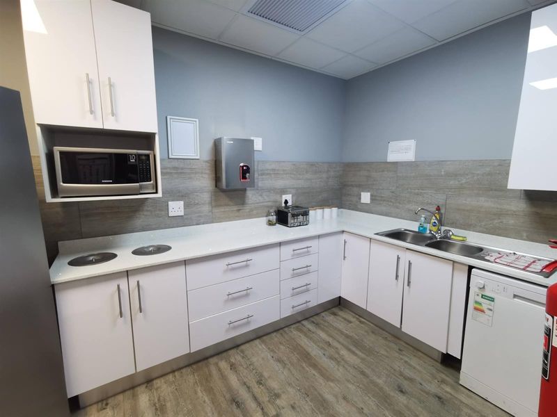 A clean and functional commercial kitchen area featuring white cabinetry, stone countertops, a double sink, and modern wood-look laminate flooring.