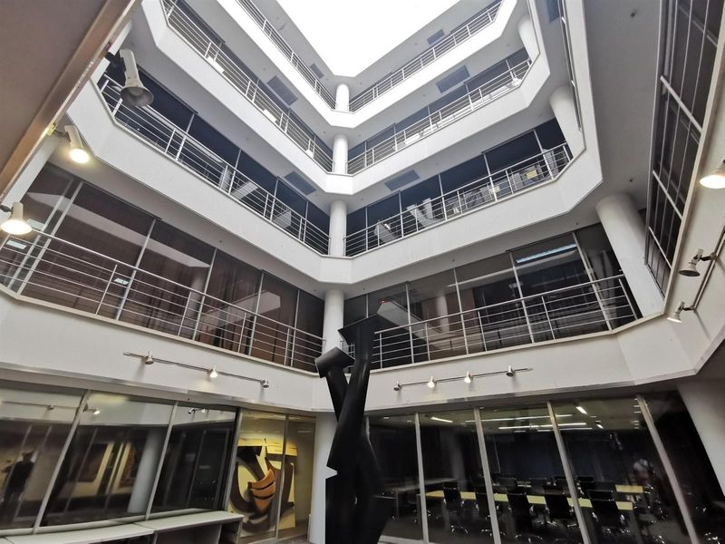 A modern commercial atrium featuring multi-level balconies, extensive glass curtain walling, and structural columns, creating an open and professional office environment.