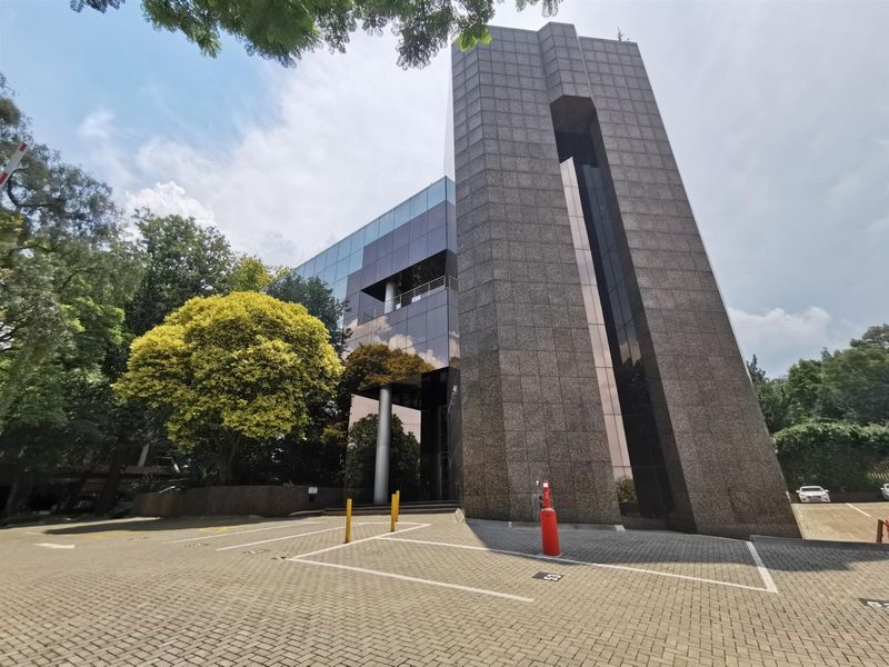 Modern commercial office building featuring a striking granite facade, extensive glass curtain walling, and a paved parking area with designated bays.