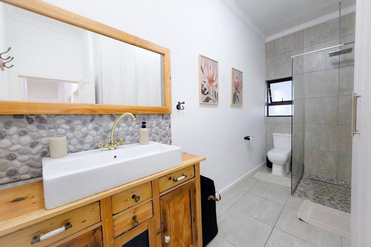 Modern bathroom featuring a rustic wooden vanity with a vessel sink, brass fixtures, and a spacious walk-in shower with pebble tile flooring.