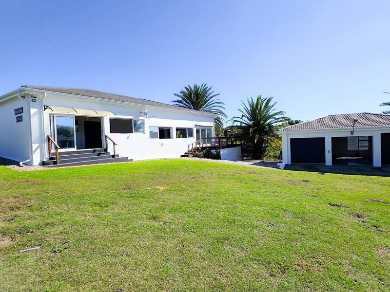 Rear view of the property featuring a spacious lawn, white exterior walls, timber decking, and a detached garage.