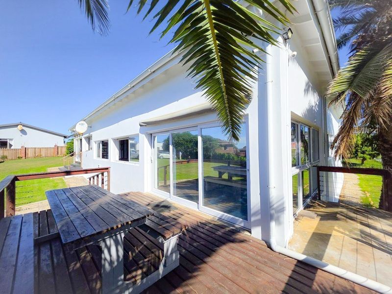 A spacious outdoor timber deck featuring sliding glass door access to the home, surrounded by a garden area.