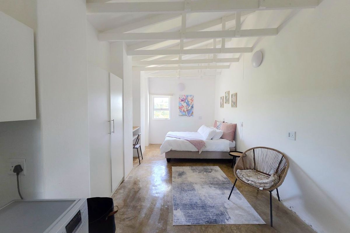 A bright bedroom featuring exposed white timber ceiling beams, polished concrete flooring, and built-in storage cupboards.