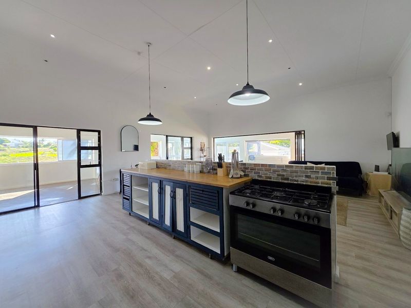 Spacious open-plan living area featuring a modern kitchen island with a gas stove, brick backsplash, and large sliding doors leading to an outdoor space.