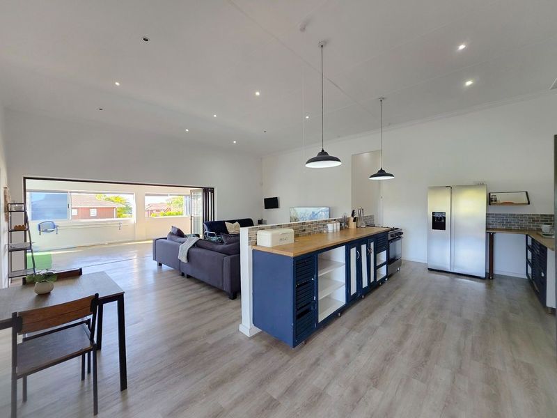 Spacious open-plan living area featuring a modern kitchen with a central island, wood countertops, and seamless flow to an outdoor patio through sliding doors.