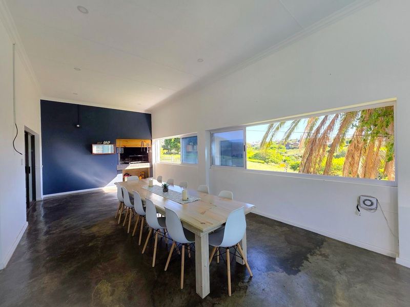 Spacious open-plan living and dining area featuring polished concrete floors, a built-in braai, and expansive windows offering scenic views.