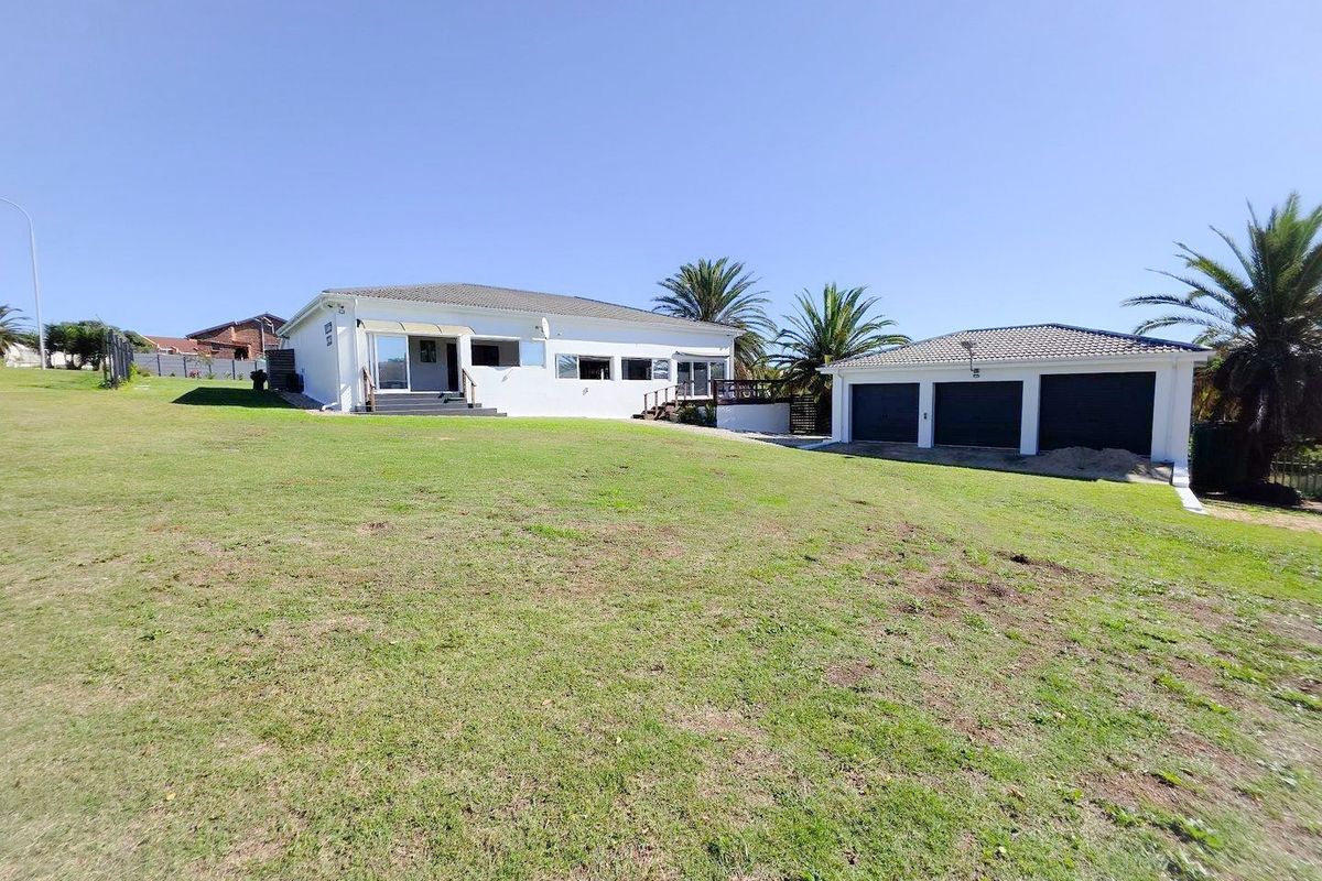 Spacious rear exterior view featuring a large lawn, a detached triple garage, and a raised deck area attached to the main residence.
