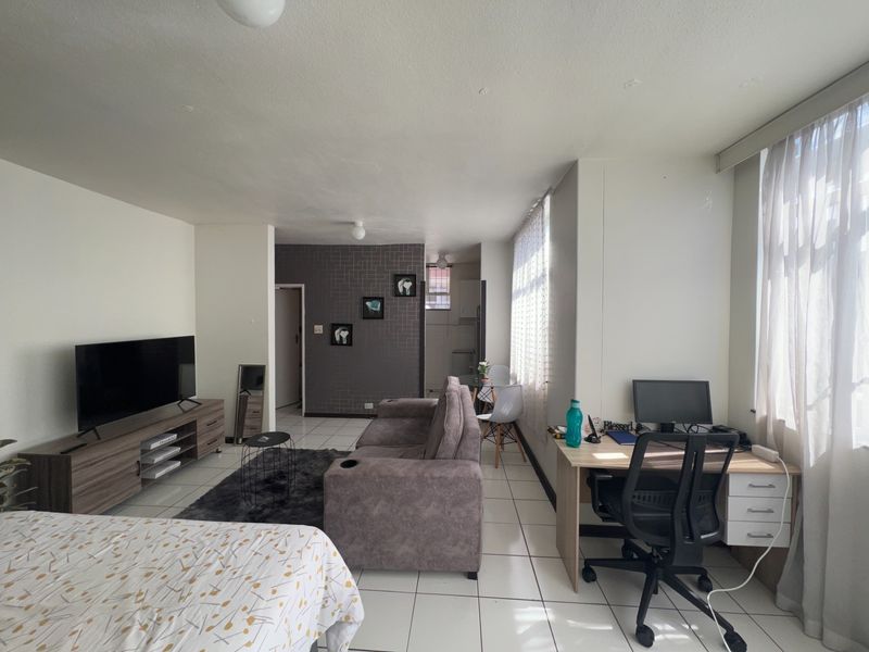 An open-plan living area featuring tiled flooring and a textured feature wall, providing a versatile space for living and workspace arrangements.