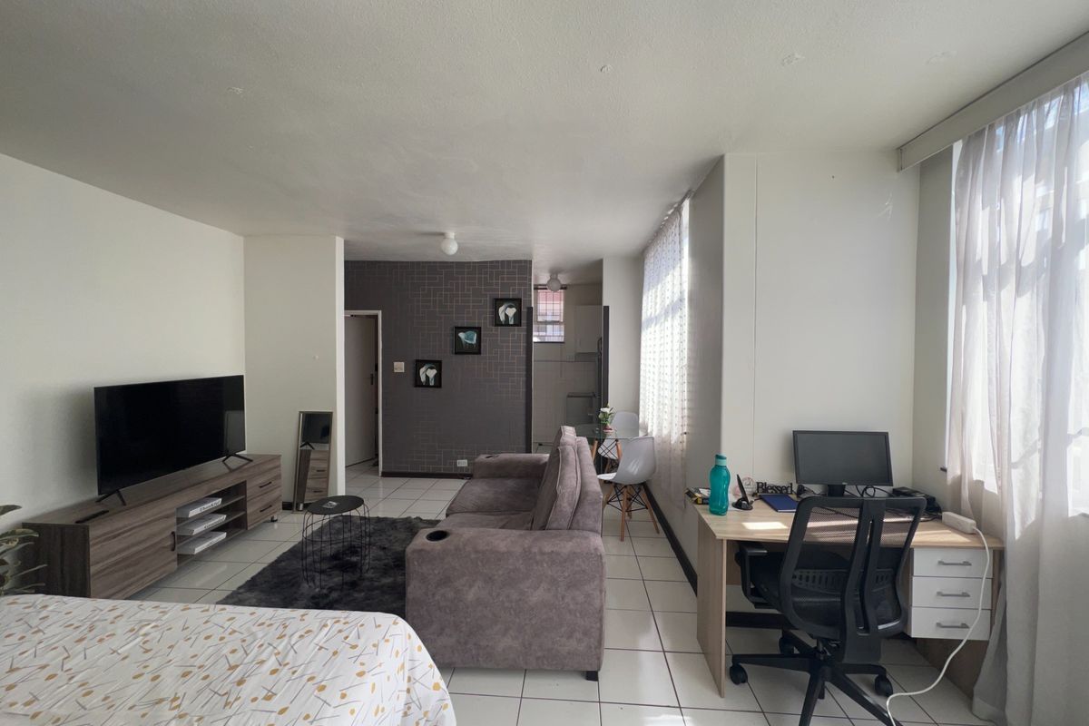An open-plan living area featuring tiled flooring and a textured feature wall, providing a versatile space for living and workspace arrangements.