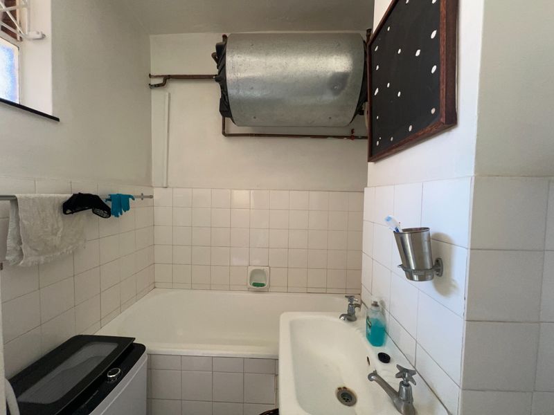 A functional bathroom featuring a bathtub, wall-mounted basin, and exposed water heater, finished with white ceramic wall tiles.