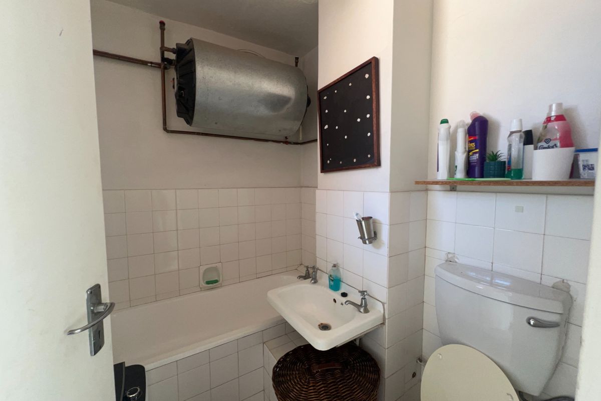 Compact bathroom featuring a bathtub, wall-mounted washbasin, toilet, and exposed water heater unit with tiled wall finishes.