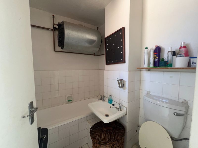 Compact bathroom featuring a bathtub, wall-mounted washbasin, toilet, and exposed water heater unit with tiled wall finishes.