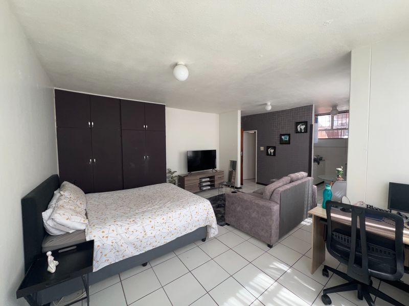A functional bedroom featuring built-in cupboards and tiled flooring, offering a practical layout with an integrated living area.