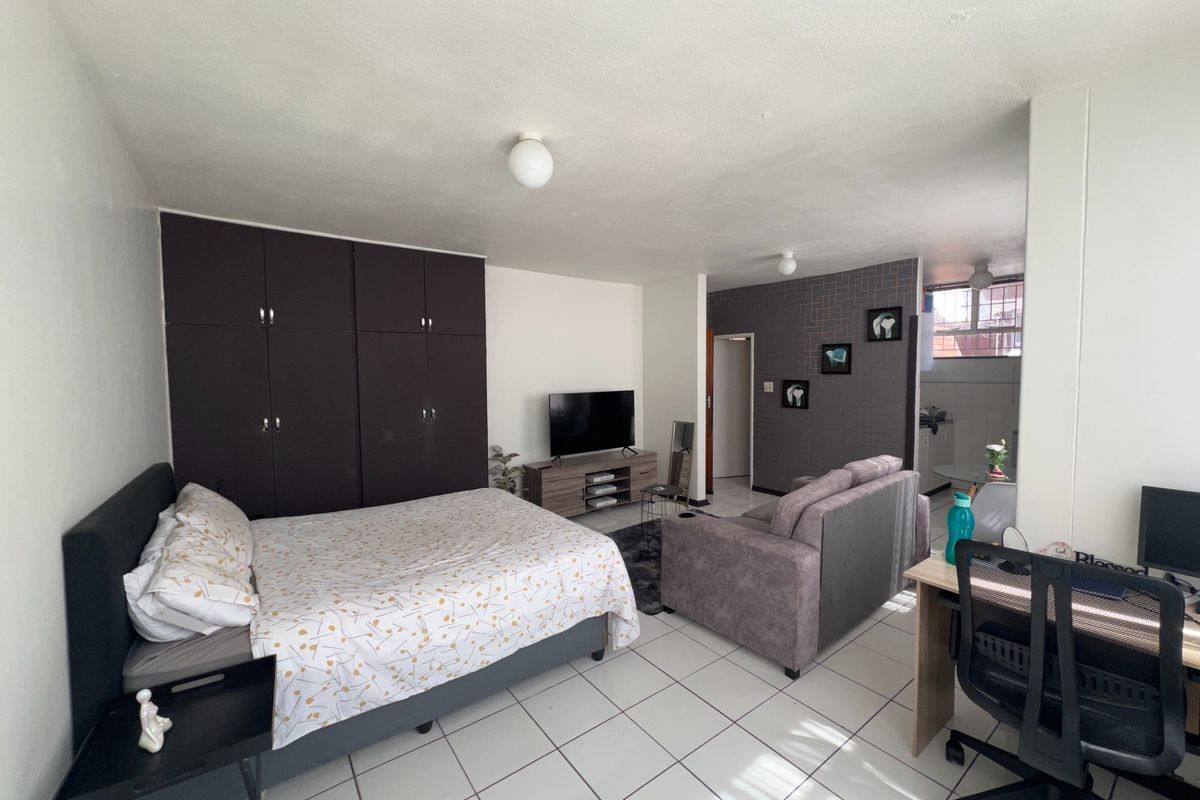 A functional bedroom featuring built-in cupboards and tiled flooring, offering a practical layout with an integrated living area.