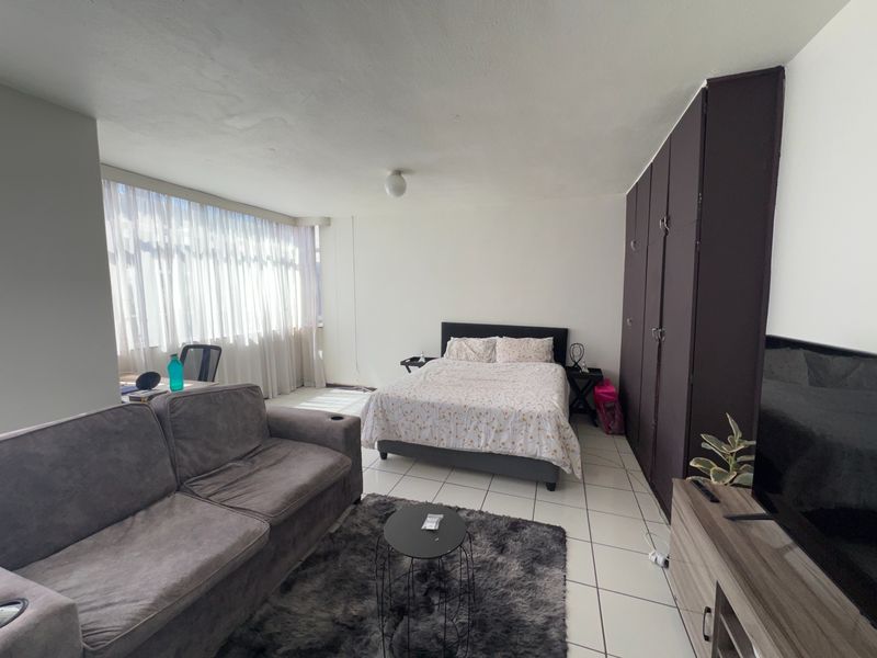 A spacious bedroom featuring tiled flooring, a large window for natural light, and a dark built-in wardrobe providing ample storage space.