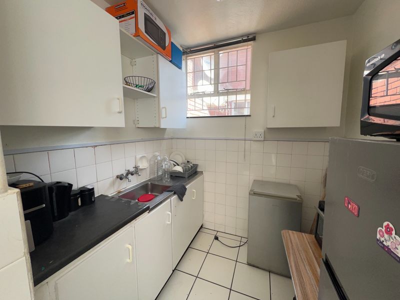 A compact scullery area featuring built-in white cabinetry, a stainless steel sink, and tiled splashbacks, providing functional utility space.