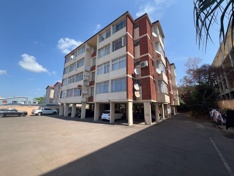 A multi-story residential apartment building featuring a brick facade, covered ground-level parking, and multiple satellite dish installations.