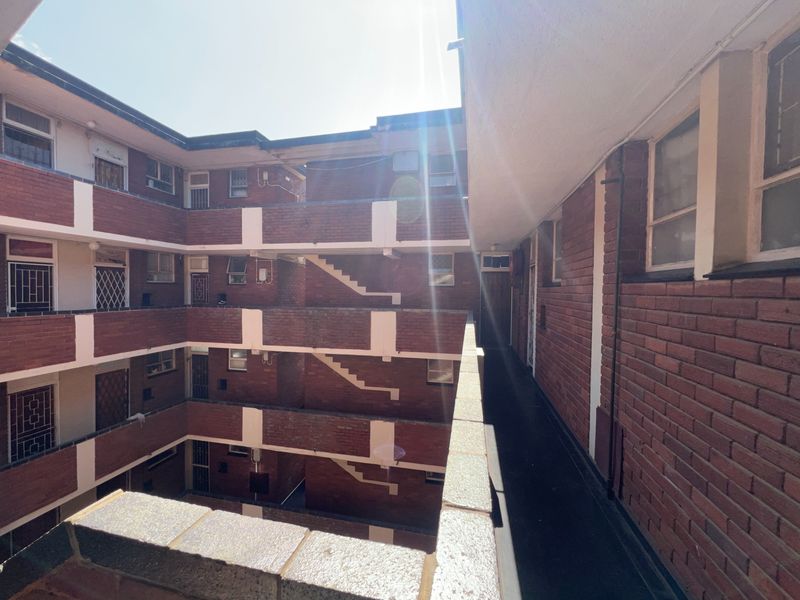 Exterior view of a multi-story apartment complex featuring brick facade, external walkways, and stairwells with security bars on windows.