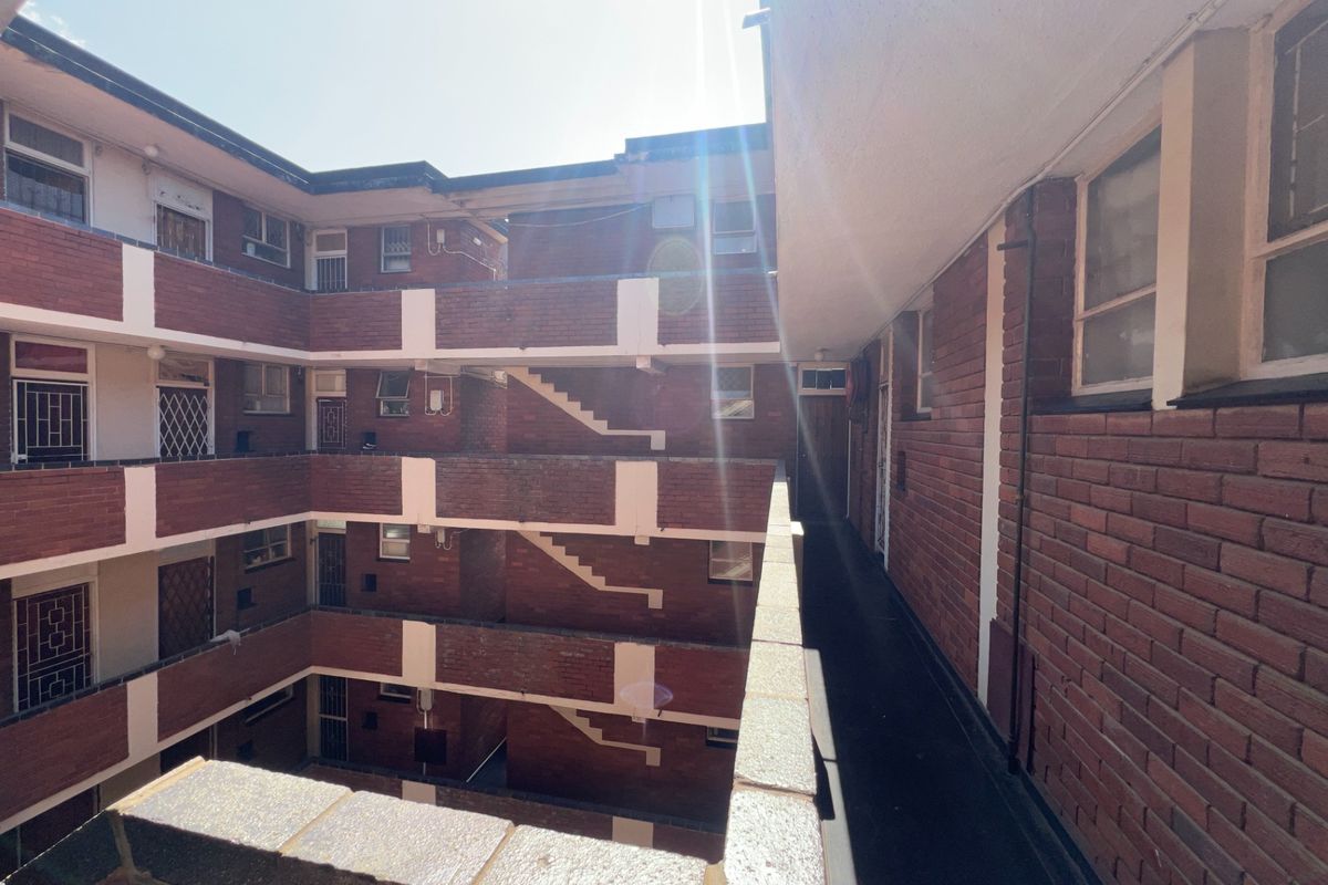 Exterior view of a multi-story apartment complex featuring brick facade, external walkways, and stairwells with security bars on windows.