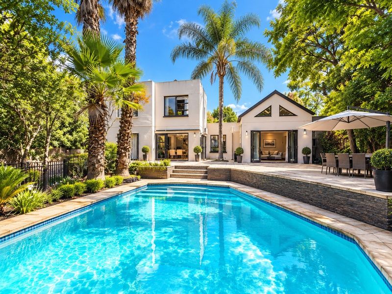 A beautifully landscaped backyard featuring a sparkling swimming pool, stone-clad retaining wall, and a spacious paved patio area perfect for outdoor entertaining.