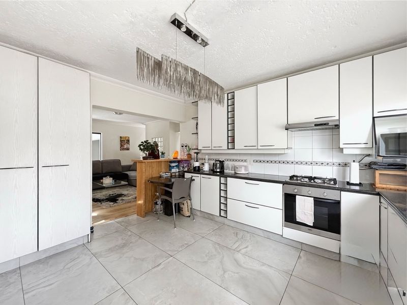 Modern kitchen featuring white cabinetry, gas hob, built-in oven, extractor fan, and large format floor tiles, with an open-plan flow to the living area.