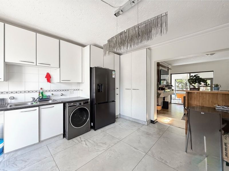 Modern kitchen featuring white cabinetry, tiled flooring, and integrated laundry space, with an open-plan flow leading into the adjacent living area.