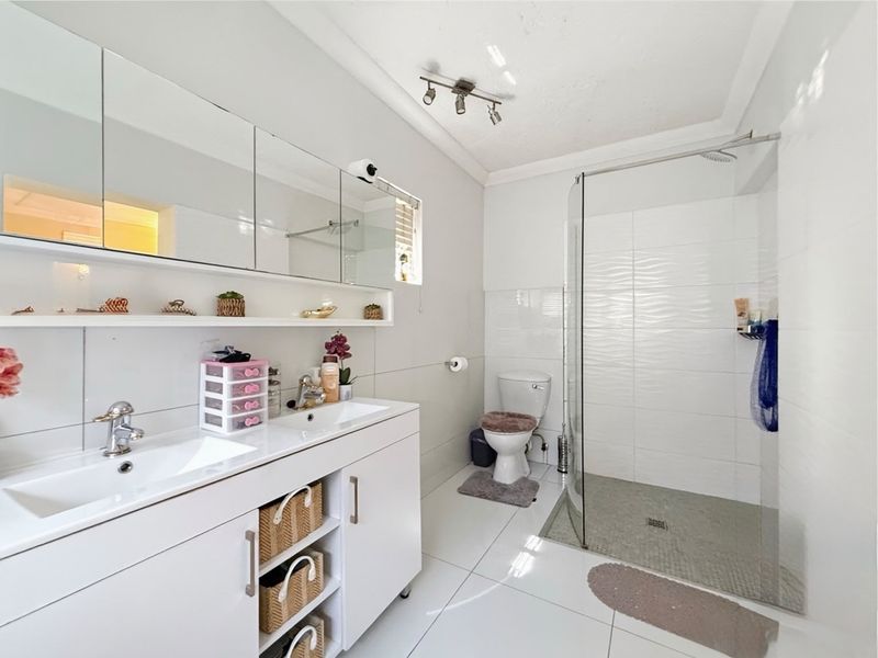 Modern bathroom featuring a double vanity with integrated sinks, a large mirrored medicine cabinet, and a spacious walk-in shower with a glass enclosure.