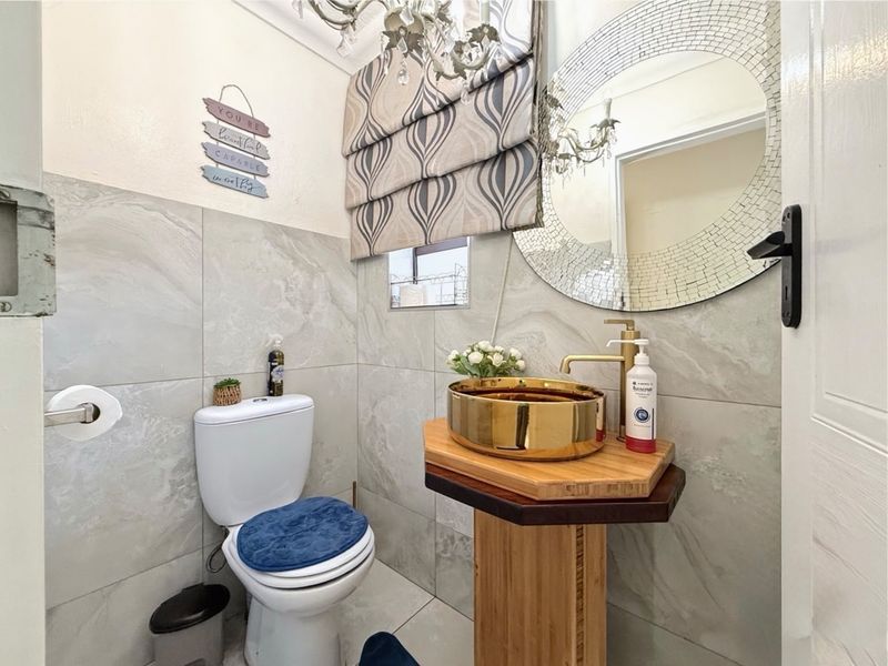 A compact, modern bathroom featuring large-format grey wall tiles, a unique wooden pedestal vanity with a gold vessel sink, and a brass faucet.