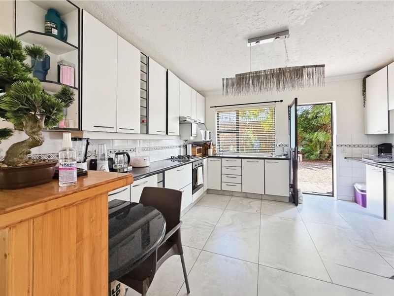 A bright, modern kitchen featuring white cabinetry, black countertops, a gas hob, built-in oven, and direct access to the rear garden area.