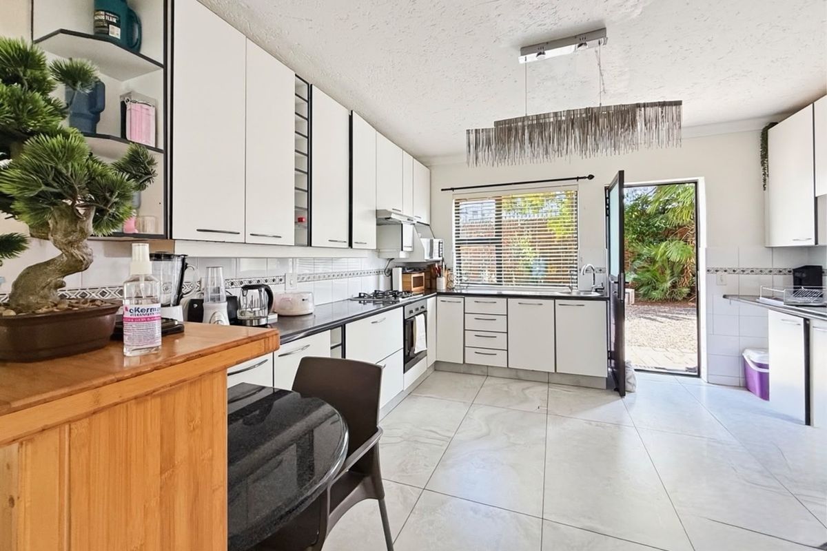 A bright, modern kitchen featuring white cabinetry, black countertops, a gas hob, built-in oven, and direct access to the rear garden area.
