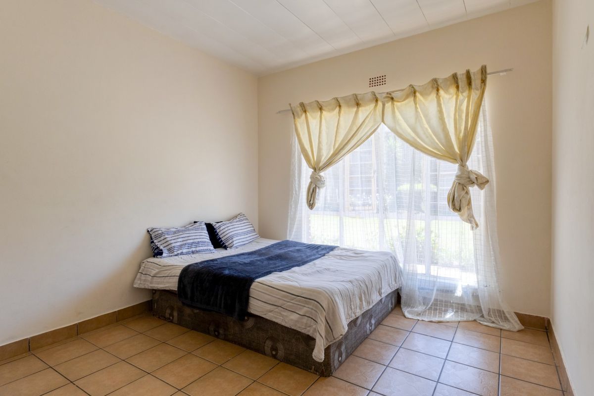 A simple bedroom featuring tiled flooring and a large window that allows for natural light.